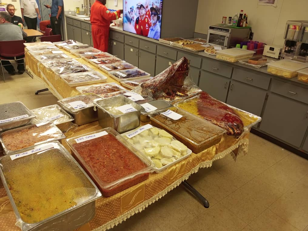 Labelled buffet spread of fried rice, jollof, egg sauce and roast meats laid out for a client mess service
